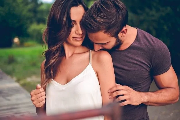 Man kissing his girlfriend in her shoulder showing that he loves her.